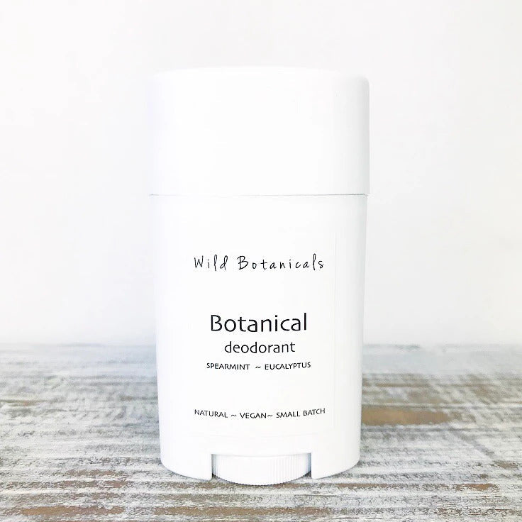 A white cylindrical aluminum-free deodorant container labeled "Wild Botanicals Eucalyptus Spearmint Deodorant" with spearmint and eucalyptus scent descriptions on a light wooden background.