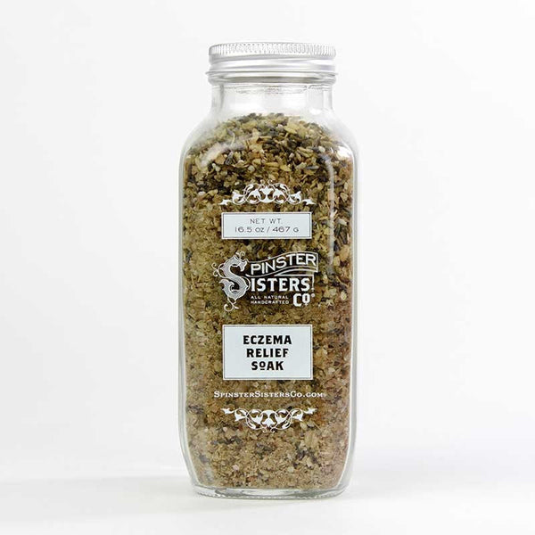 A clear glass jar filled with a mixed herbal blend labeled "Spinster Sisters Co. Eczema Relief Soak." The jar contains colloidal oatmeal and is sealed, displaying product details on a card attached to the lid.