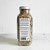 A Spinster Sisters Eczema Relief Soak jar filled with whole spices on a plain background, featuring a white label with black text indicating spice names and possibly other information about colloidal oatmeal.