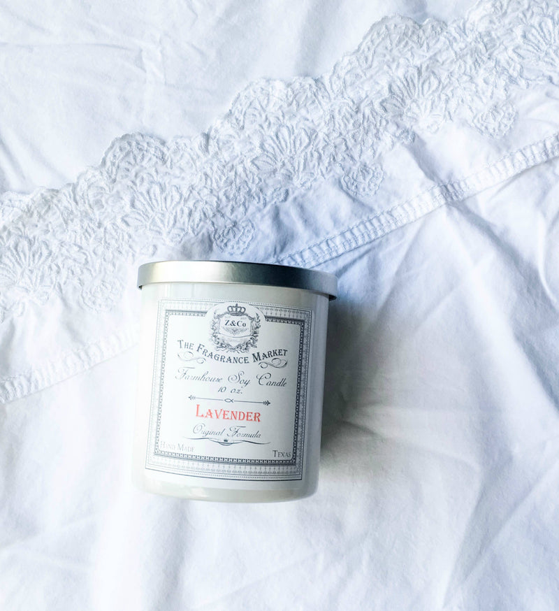 A Z&Co. Lavender Farmhouse Candle sitting on a white lace fabric. The label displays elegant typography and an emblem, emphasizing a vintage aesthetic. Made from natural vegetable wax, it offers a pure and