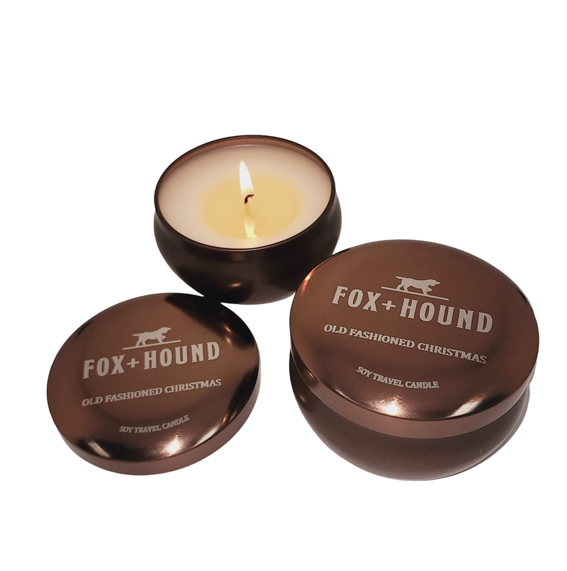 Three scented, odor-eliminating candles from Fox + Hound with one lid open, showing a lit candle, and two closed, labeled "Fox + Hound Old Fashioned Christmas Travel Soy Candle 7 oz.