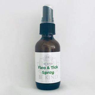 A brown spray bottle with a blue cap. The label reads "Be Kind Pet Line - Flea and Tick Spray" in green and black text with a floral graphic, ideal for outdoor pet care.