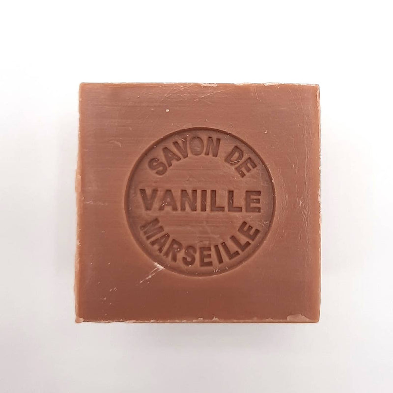 A bar of vanilla-scented Senteurs De France Marseille Vanilla Cube Soap enriched with shea butter, in a light brown color, with embossed text on its surface reading "savon de vanille Marseille." The background is