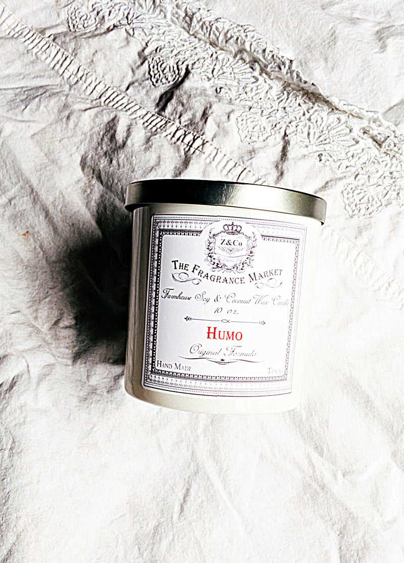 A cylindrical Z&Co. Humo Farmhouse Candle with additional text, "lavender & white tea chai," on a textured white fabric background, crafted from natural vegetable wax.