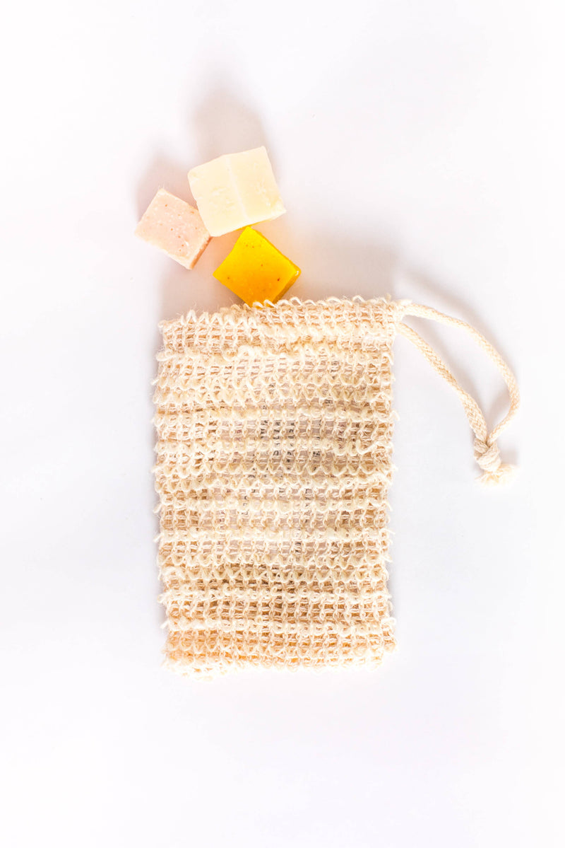 Three bars of soap next to a SOAK Bath Co. sustainable sisal exfoliating bag on a white background.