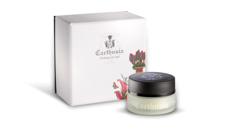 A Carthusia I Profumi de Capri branded skincare product with its packaging. The packaging is white with a colorful floral print featuring wild carnations, and the product, a small jar with a black lid, is displayed in.