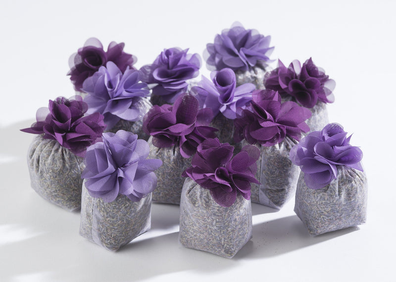 A row of small, silver Sonoma Lavender Flower Sachets filled with lavender scent, topped with decorative purple fabric flowers, arranged on a white surface.
