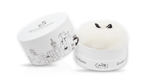 A round white box with black cityscape line art and "Carthusia I Profumi di Capri" and "Capri" on the lid holds fluffy dusting powder in Forget Me Not scent—luxury from Carthusia Capri Forget Me Not Dusting Powder.