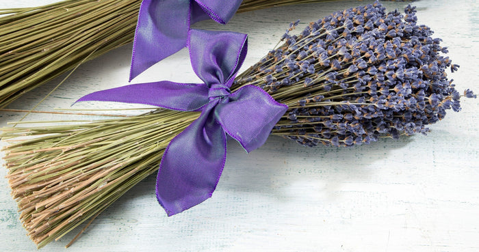 A bundle of Sonoma Lavender Bouquets tied with a purple ribbon, resting on a faded white wooden surface.
