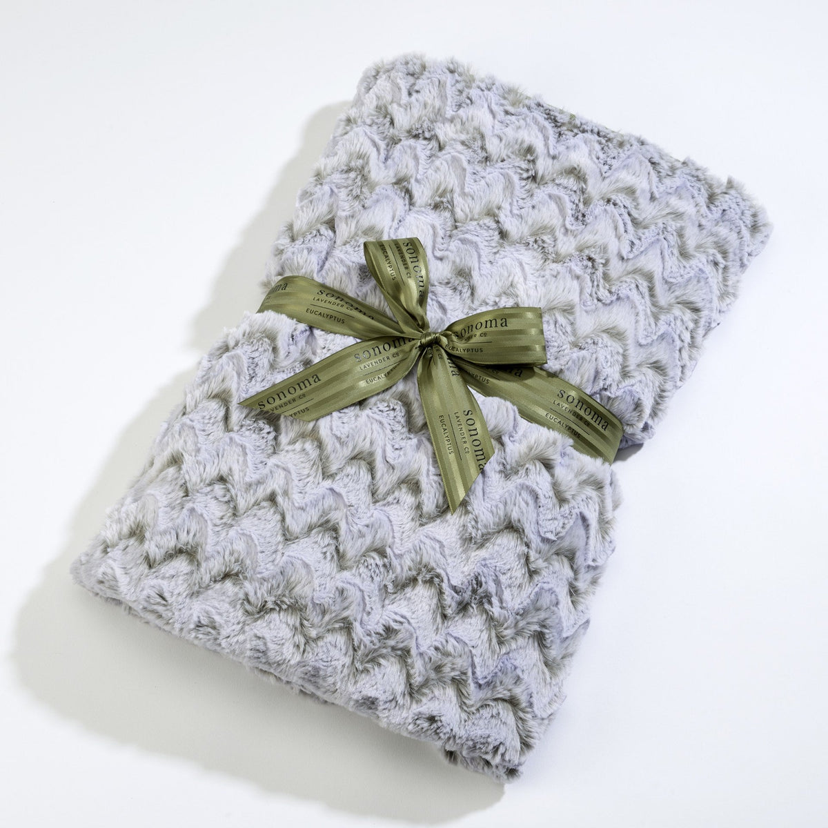 A Sonoma Lavender knitted scarf with a textured pattern, neatly folded and tied with a shiny olive green ribbon featuring gold text, infused with eucalyptus lavender.