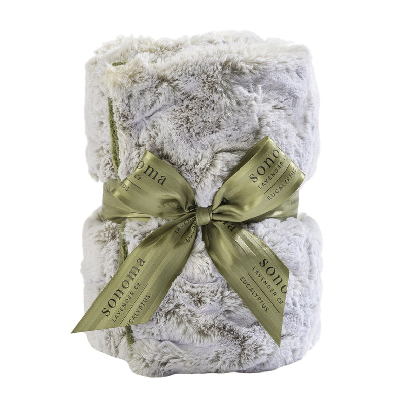 A plush, folded white and gray blanket tied with an olive green ribbon labeled "Sonoma Eucalyptus Frosted Moss Heat Wrap" on a white background.