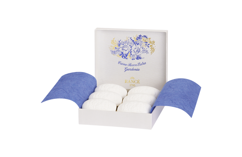 A luxurious white Rancé box open displaying three Rancé Classic Soap - Gardenia oval soaps, nestled in blue tissue paper, with a gold and blue floral design on the inside cover titled "grande herbes de la