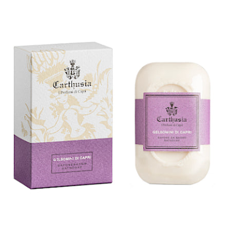 Image of a Carthusia Gelsomini di Capri Bath Soap solid soap bar next to its packaging. The soap is white with a purple label, and the box has a light floral design and purple detailing.