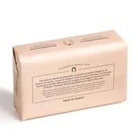 A bar of Fer à Cheval Gentle Perfumed Soap Bar - Olive Blossom, wrapped in elegant pastel pink paper, featuring French text, a vintage logo, and "made in France" label, isolated on a white background.