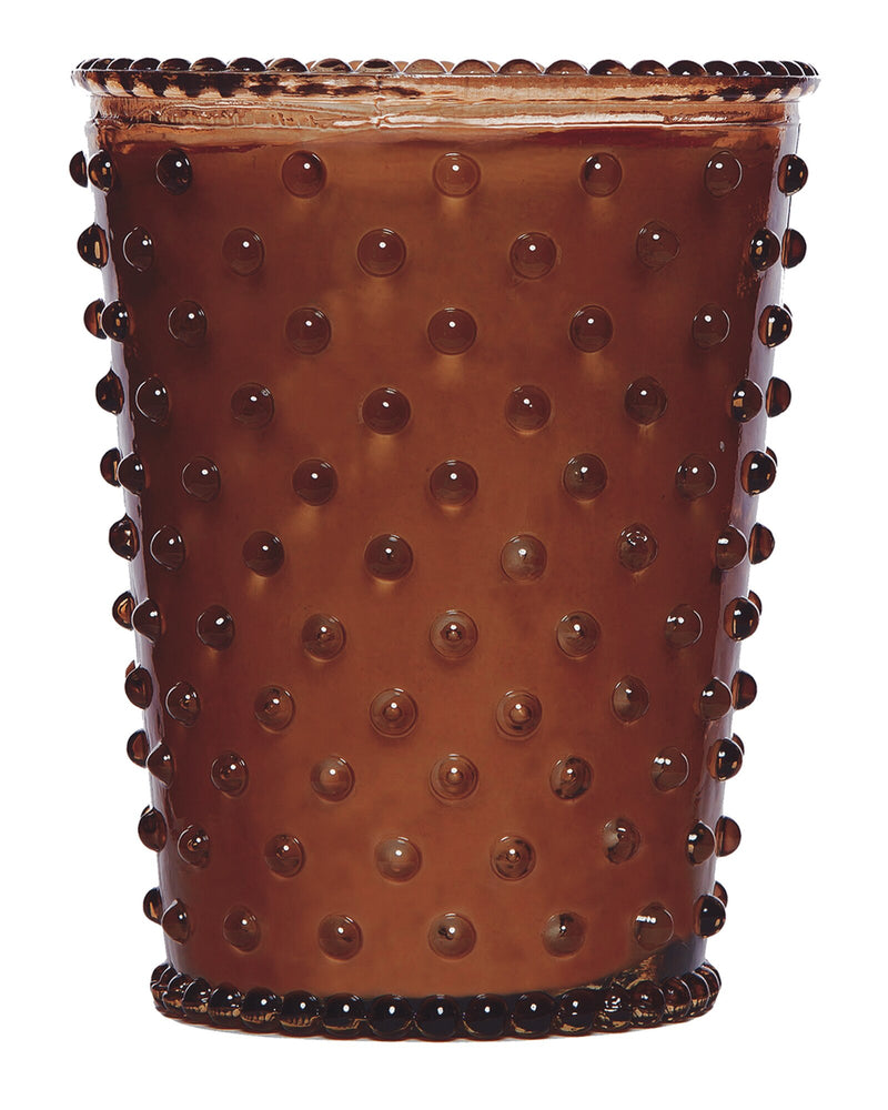 A close-up view of a brown, textured ceramic pot with a pattern of raised dots covering its surface. The top edge is slightly irregular, adding a rustic charm, ideal for housing a hand-poured Simpatico NO. 69 Gingerbread Hobnail Glass Candle.