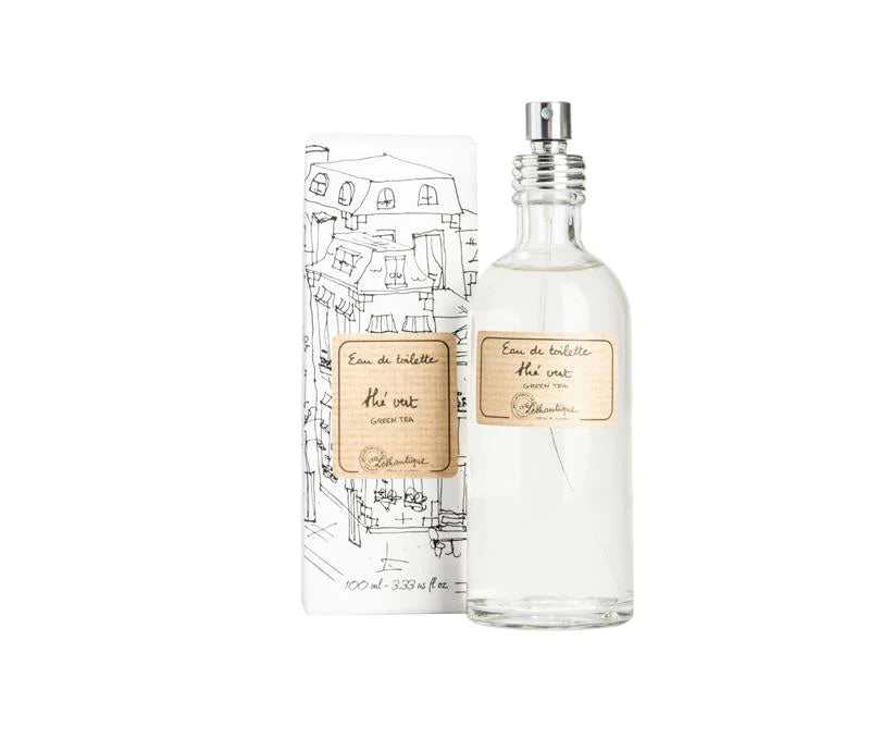 A bottle of Lothantique Green Tea Eau de Toilette with a clear body and a spray nozzle, next to its packaging featuring sketch-like illustrations of a cityscape. The label indicates it is scented with lemon jasmine.