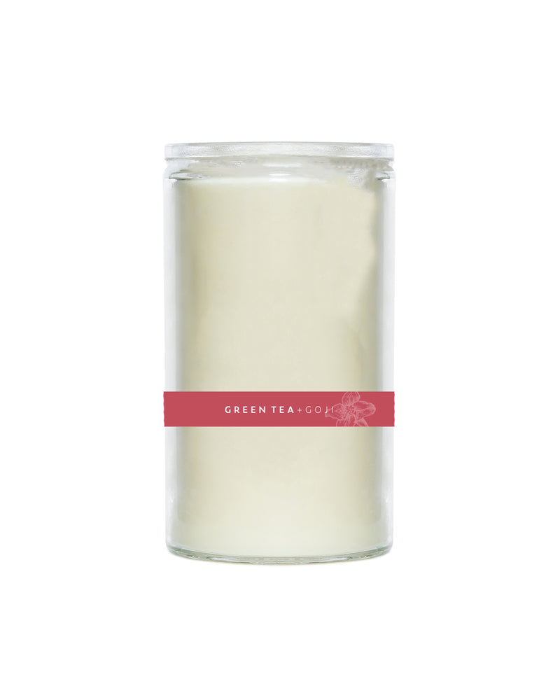 A cylindrical white U.S. Apothecary Green Tea + Goji Berry Candle in a clear glass jar, labeled "green tea & goji berries" with a decorative floral design on a burgundy label.