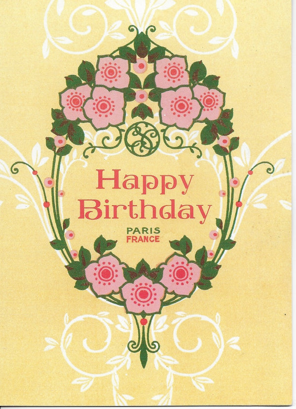 A Greeting Cards birthday greeting card with the text "happy birthday" in pink, centered in a decorative floral wreath with symmetrical roses and leaves, against a yellow background. Below the text is "Paris France".