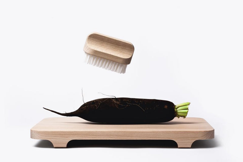 A black radish and an Andrée Jardin "Canot" Vegetable Brush Hard placed on a light wooden tray against a white background.