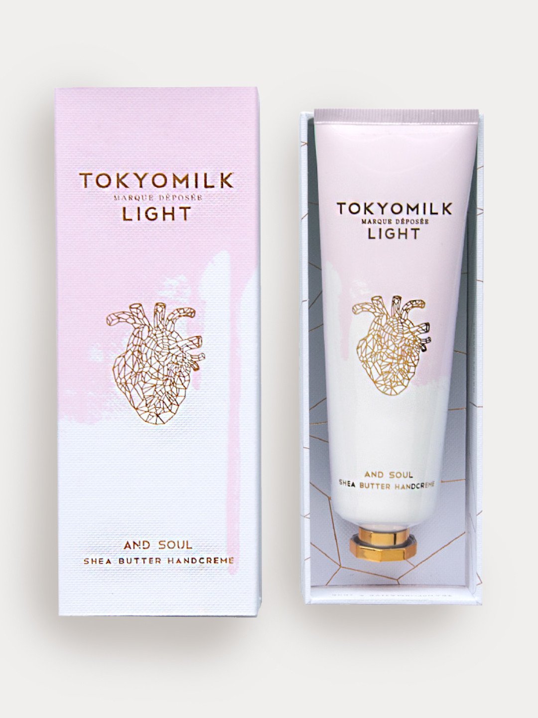 A tube of Margot Elena TokyoMilk Light And Soul No. 01 shea butter hand cream next to its packaging box, both featuring an artistic, golden anatomical heart design on a pale pink background.