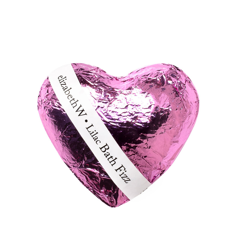 A shiny, metallic pink elizabeth W Fizz Heart - Lilac bath bomb wrapped in crinkled foil with a white label inscribed with "elizabethW lilac bath fizz.
