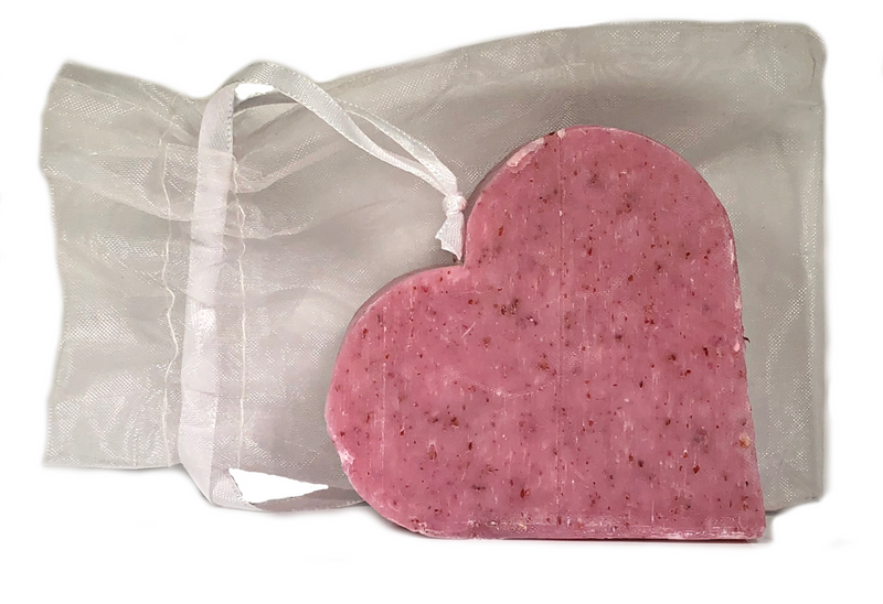 A pink Massalia Heart Soap - Grapefruit Exfoliating bar with speckles, placed beside a sheer white drawstring bag on a white background.