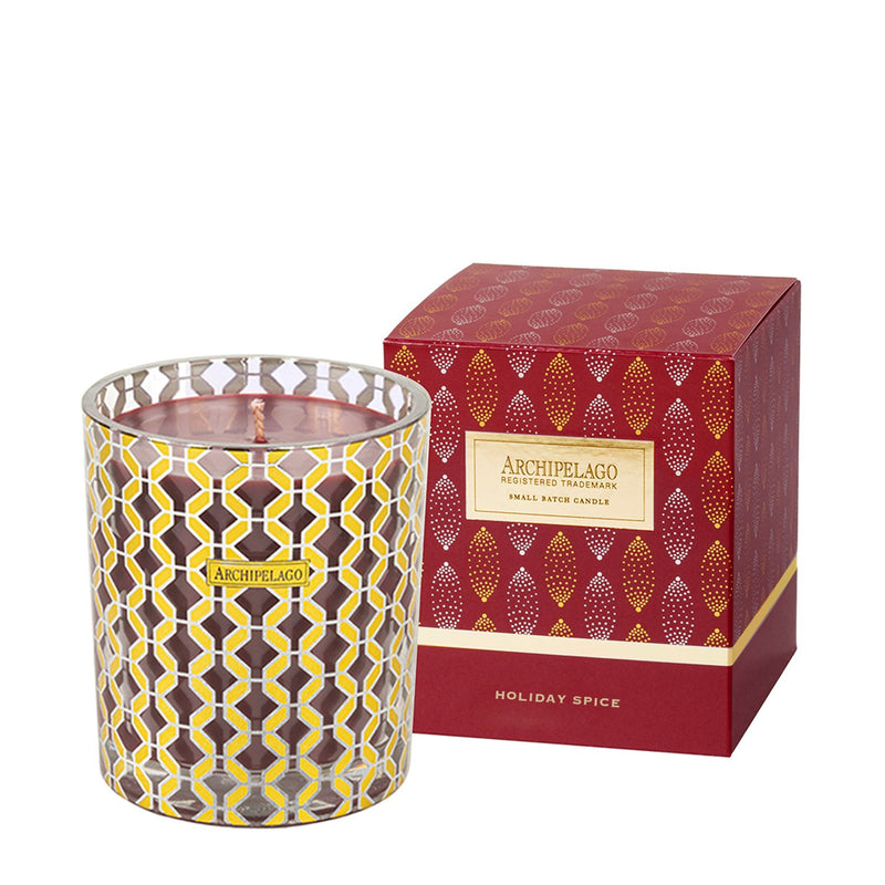 A scented candle in a decorative glass holder beside its matching Archipelago Holiday Spice Gift Box Candle with a vanilla, cassis, and clove fragrance.