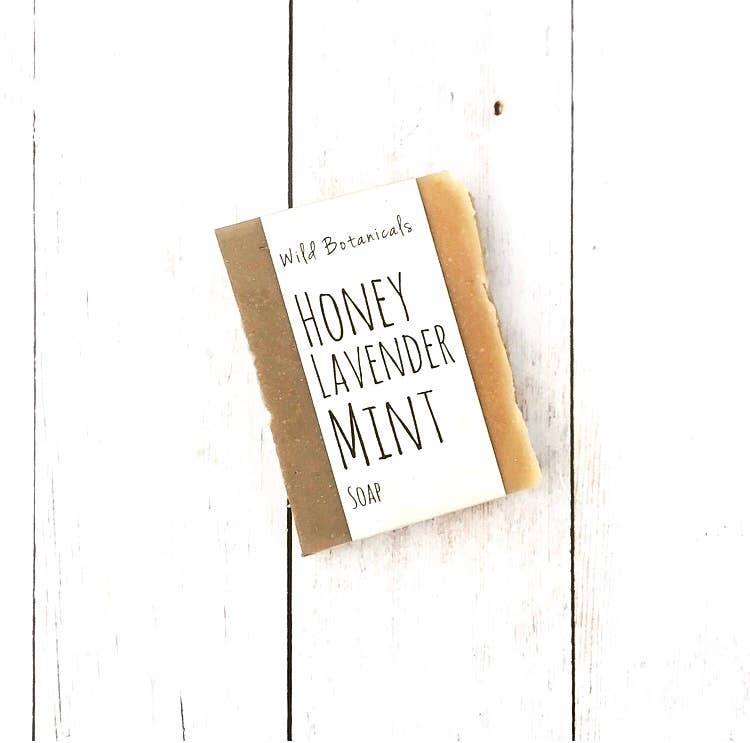 A bar of Wild Botanicals Honey Lavender Mint soap, resting on a rustic white wooden surface.
