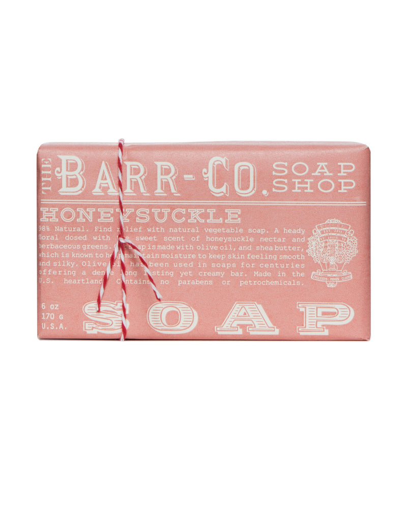 A packaged bar of Barr-Co. Honeysuckle Triple Milled Bar Soap, wrapped in pink paper with white textual details and secured with a red and white striped twine.
