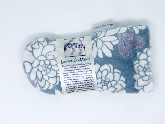 A pair of Sonoma Lavender Ibiza Spa Mittens with a floral design laid out on a white background, featuring attached labels describing the product's heat therapy and calming properties.