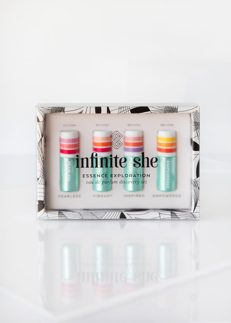 A boxed set of Margot Elena's Infinite She Essence Exploration Eau de Parfum Discovery Set, featuring four small vials in pink, white, and turquoise, displayed on a reflective white surface.