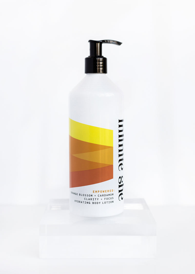 A pump bottle of Margot Elena's Infinite She Empowered Hydrating Body Lotion, featuring a gradient yellow label with text and Orange Blossom, on a white background.
