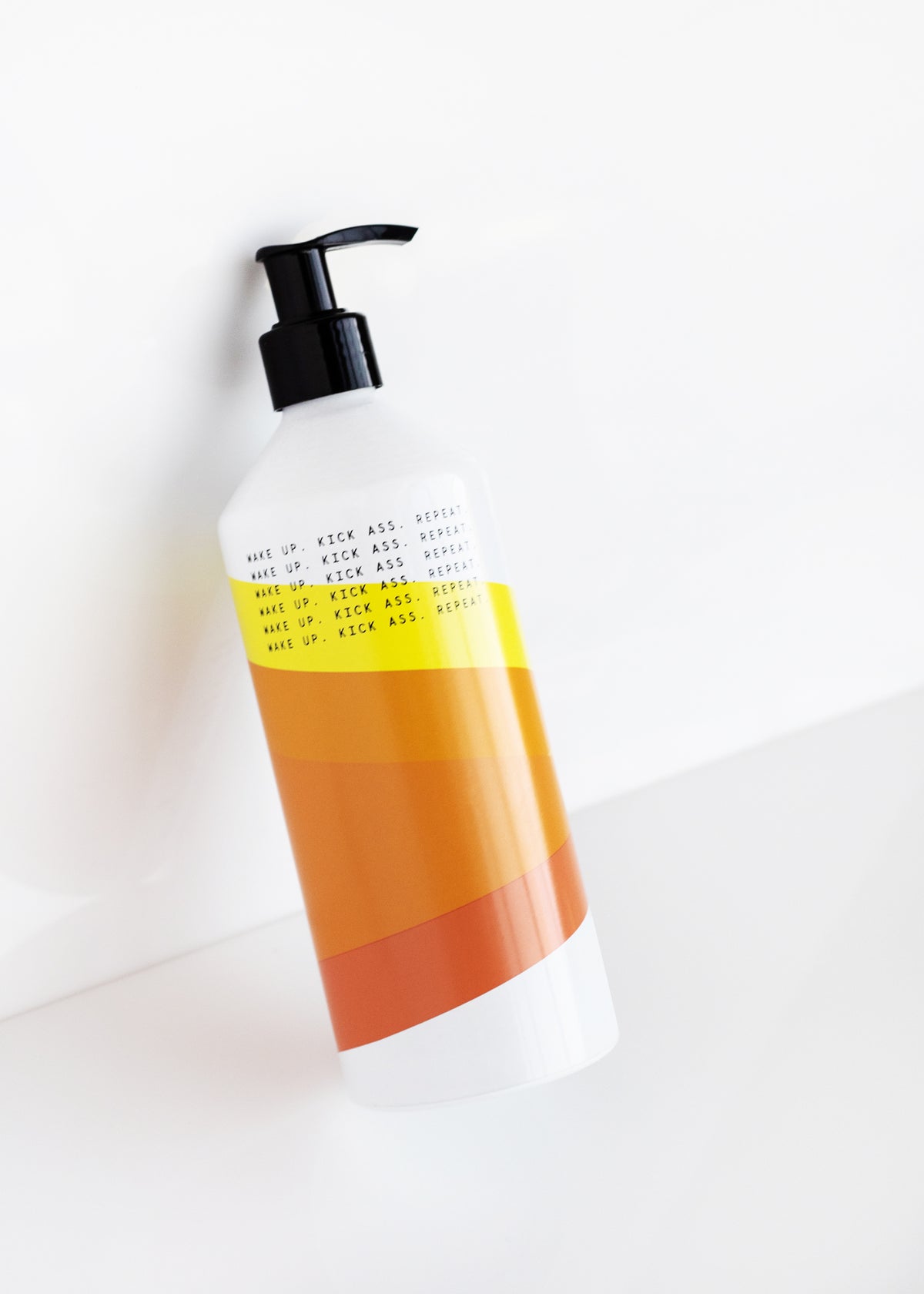 A Margot Elena dispenser bottle with a pump, featuring colorful horizontal stripes in shades of yellow and orange with hints of orange blossom, set against a plain white background.