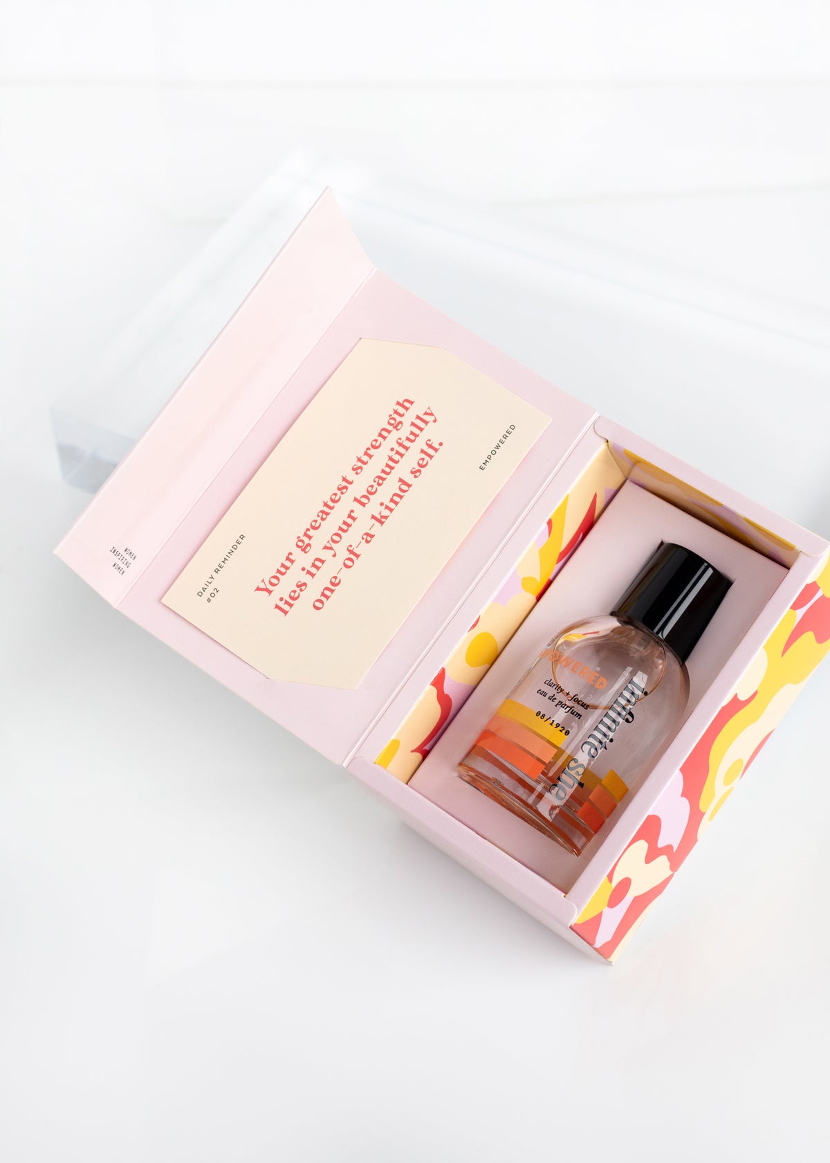 A Margot Elena Infinite She Empowered Eau de Parfum in a colorful box with a motivational quote on the inside lid, placed on a white surface.
