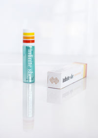 Two Infinite She Empowered Rollerball Eau de Parfum by Margot Elena on a reflective white surface: a vertical tube with a teal, orange, and yellow design on the cap and a horizontal box with an orange blossom pattern.
