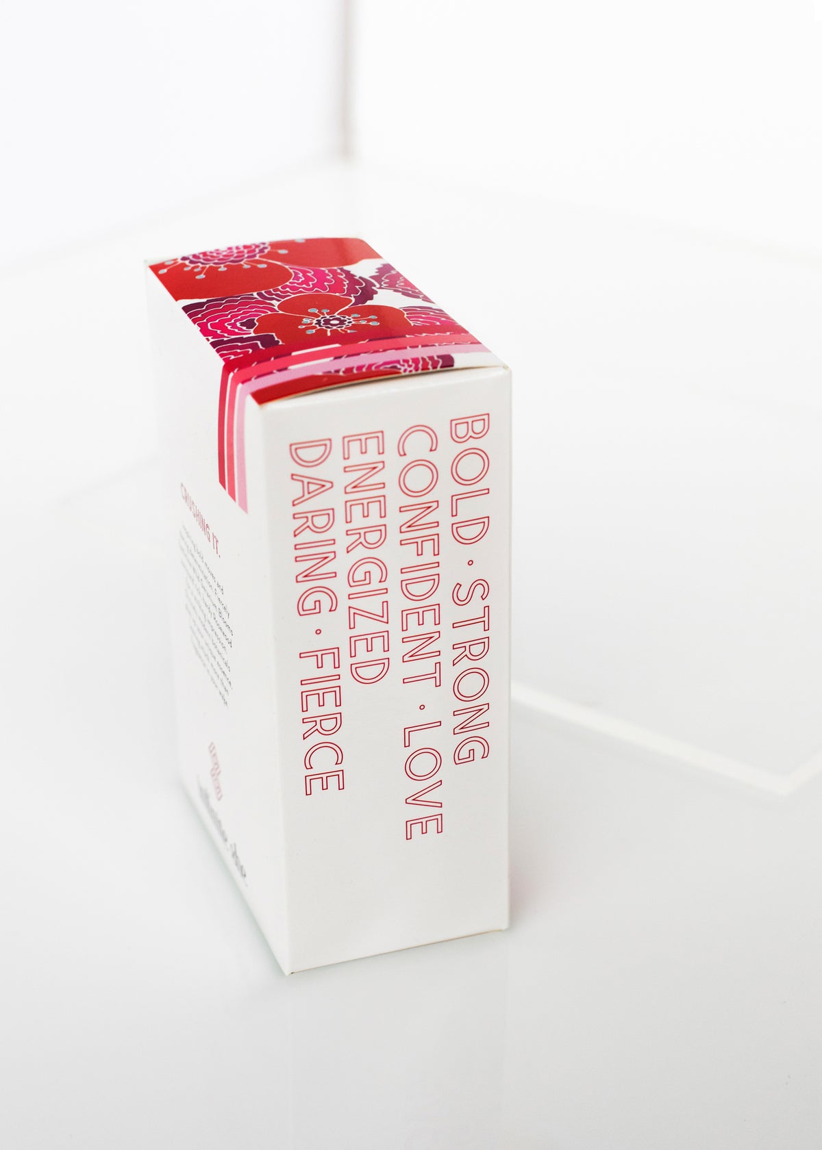 A white Margot Elena product box on a glossy surface with the words "bold, confident, strong, energized, love, daring, fierce" and "Vegan Fragrance" printed in black and red fonts.