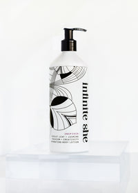 A bottle of Margot Elena's "Infinite She Inspired Hydrating Body Lotion" with an artistic black and white design on a white background, featuring abstract line art and text detailing the product's inspiration, scent, and vegan skincare formulation.