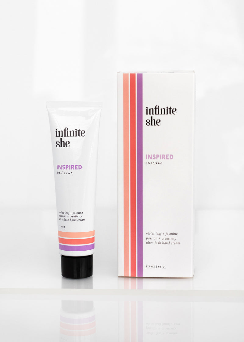 A tube of Margot Elena's Infinite She Inspired Ultra-Lush Hand Cream labeled "051194" next to its packaging box with violet leaf and jasmine details, displayed against a white background.