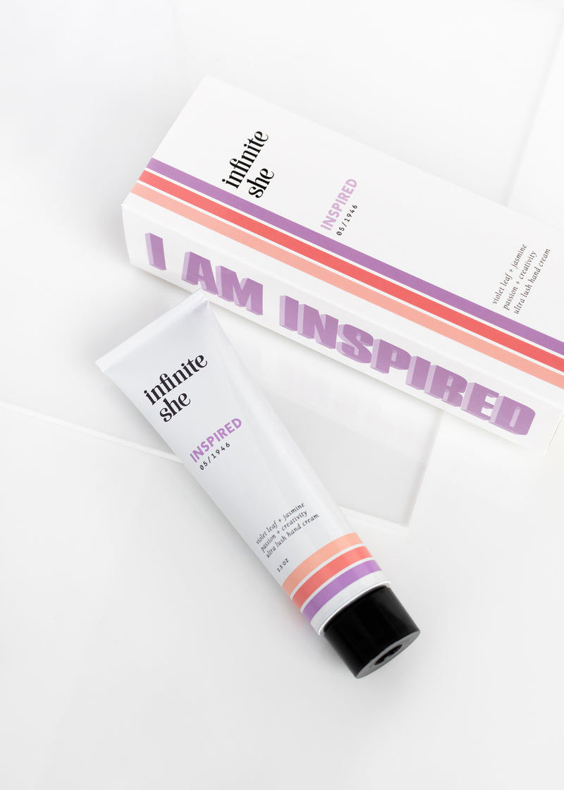 Skin cream tube labeled "Infinite She Inspired Ultra-Lush Hand Cream" and its matching box with "Shea Mango Butters inspired" text, both displayed on a white surface with a slight shadow.