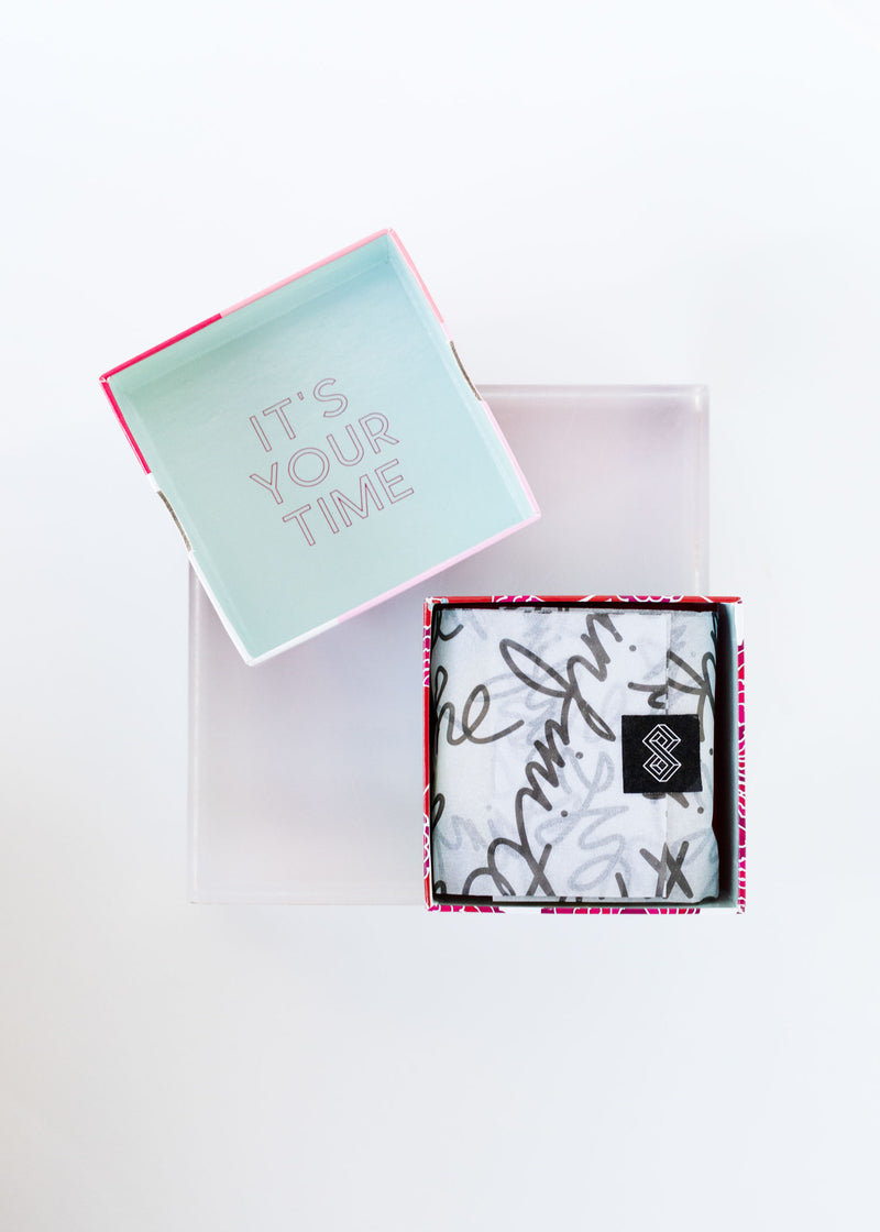 An open gift box with the lid featuring the message "it's your time" placed beside it, and an Infinite She One Badass Babe Shea Butter Soap with a pattern inside the box set against a white background by Margot Elena.