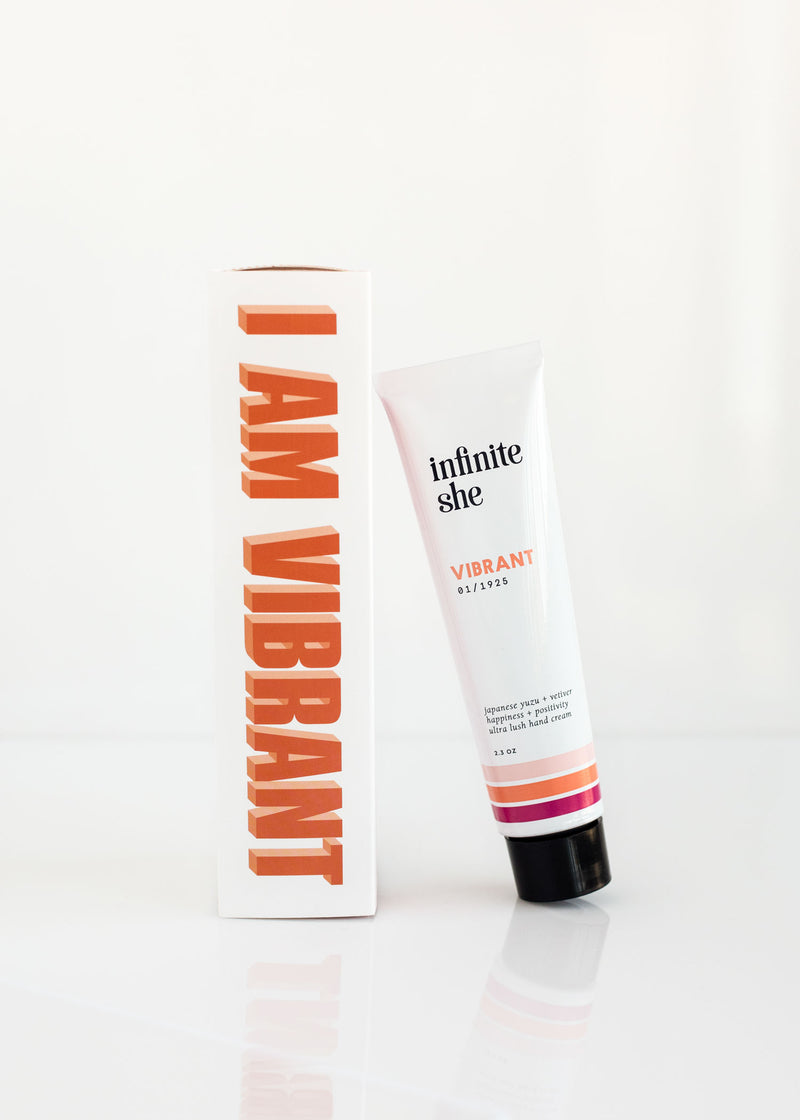 A tube of Margot Elena's "Infinite She Vibrant Ultra Lush Hand Cream" infused with Shea + Mango Butters next to its packaging box with "i am vibrant" text, set against a clean white background.