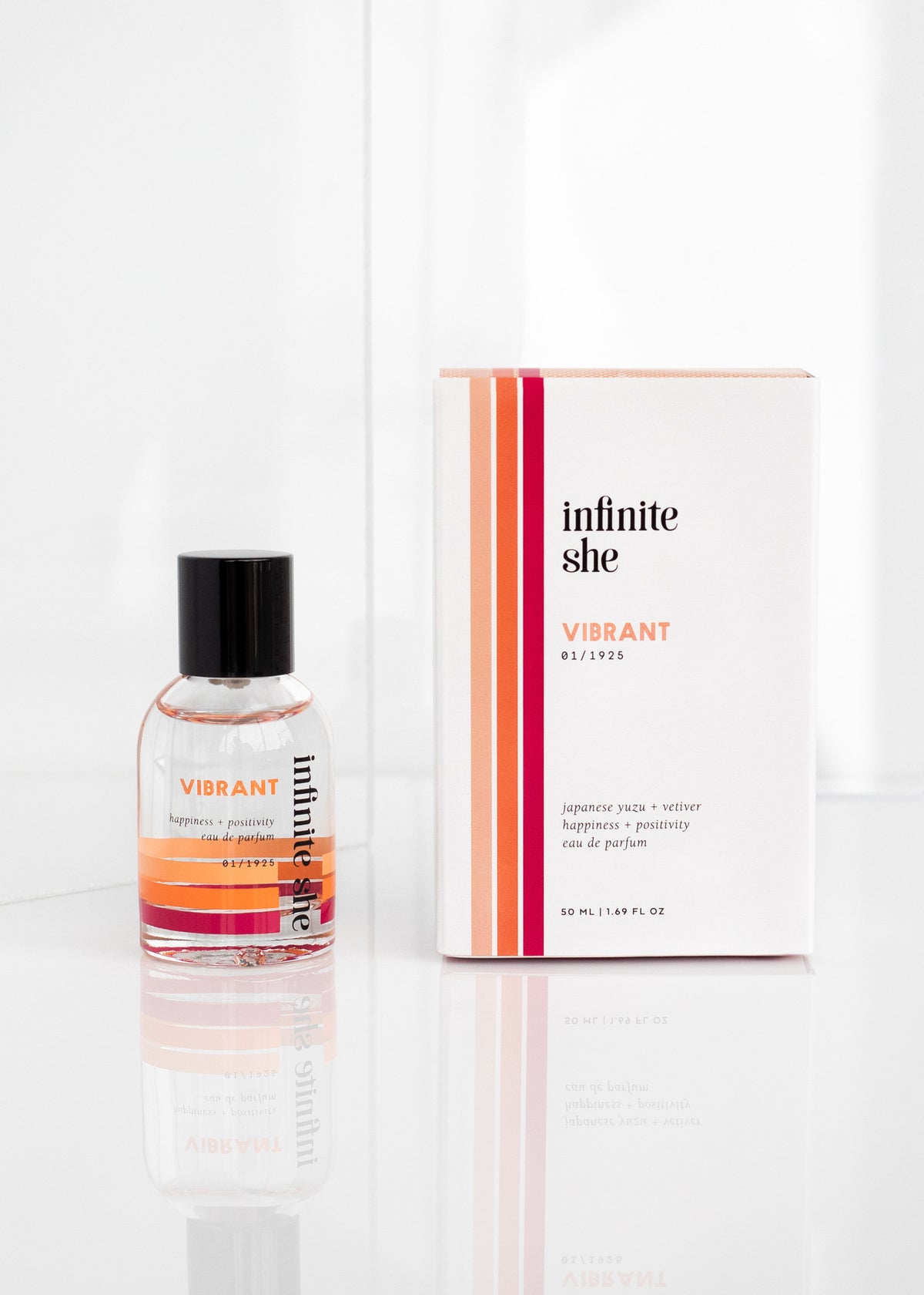 A Margot Elena cosmetic product, "Infinite She Vibrant Eau de Parfum," placed on a reflective surface. The package is white with orange and pink stripes, alongside a clear bottle with a matching label that subtly highlights the essence of.