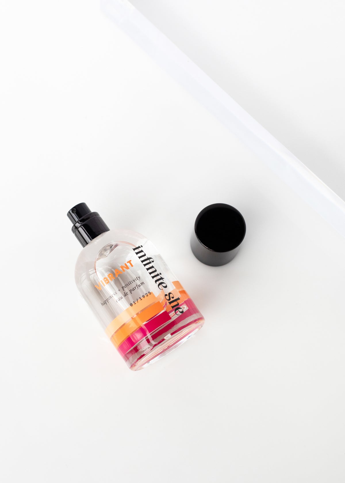A bottle of Margot Elena's Infinite She Vibrant Eau de Parfum lies on a white surface next to its black cap, angled against a minimalistic background.