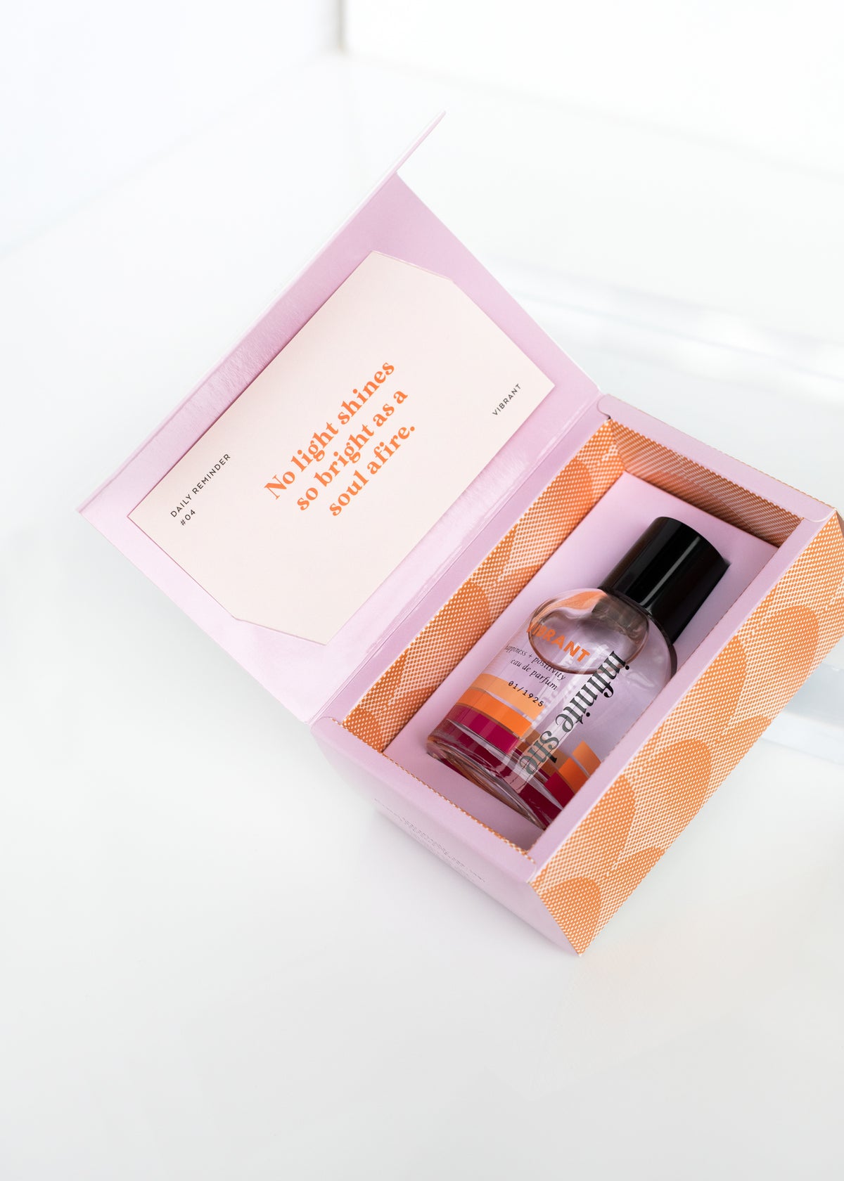 A Margot Elena beauty product box containing a bottle of Infinite She Vibrant Eau de Parfum, opened to reveal a vibrant pink interior with a Fresh Inspiration Card, resting on a white surface.