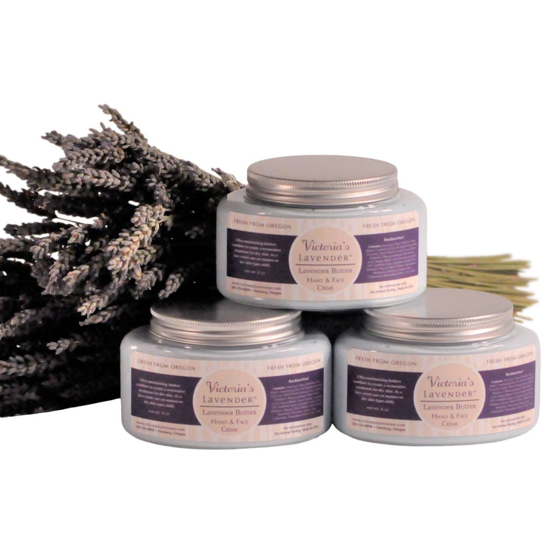 Four jars of Victoria's Lavender - Lavender Butter Face & Hands 8oz arranged in a semi-circle with a bouquet of dried lavender on the left, on a plain background. The labels indicate the balm is for hands and feet.