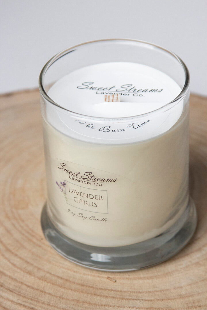 A Sweet Streams Lavender Co. lavender citrus scented soy candle, displayed on a wooden slice, with the candle's white wax and brand label visible.