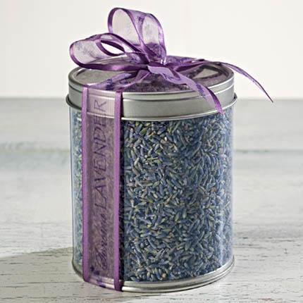 A clear cylindrical container filled with culinary grade Sonoma Lavender Botanicals flower buds, sealed with a lid and adorned with a decorative purple ribbon tied into a bow, and a label saying "lavender.