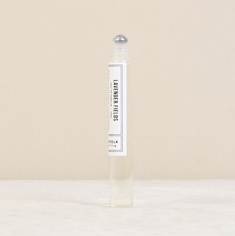 A clear rollerball perfume bottle labeled "Norfolk Natural Living Parfum de l'eau Lavender Fields" standing on a neutral beige background. The oil-based parfum inside appears almost colorless.