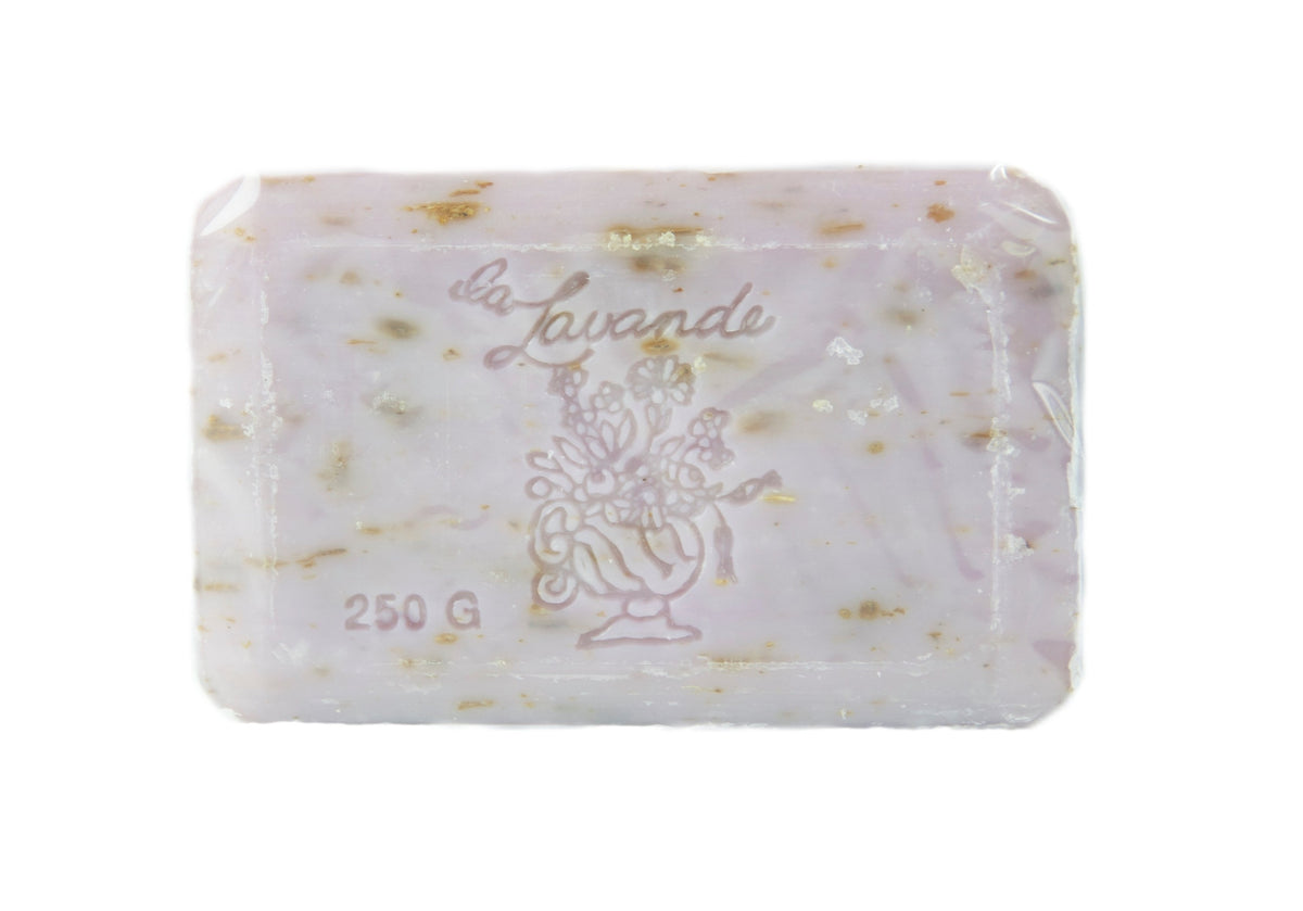 A bar of La Lavande Lavender Lilac soap labeled "La Lavanda" with flecks of herbs embedded within, weighing 250 grams. The soap is translucent and square-shaped, isolated on a white background.