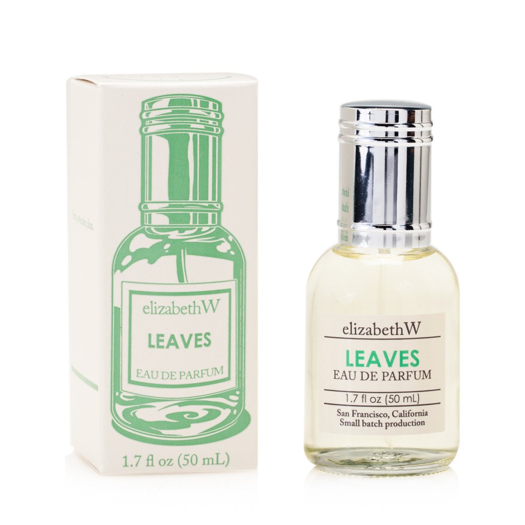 A bottle of elizabeth W Small Batch Apothecary Leaves Eau de Parfum next to its packaging box, isolated on a white background. The bottle is transparent with a green label and silver cap.